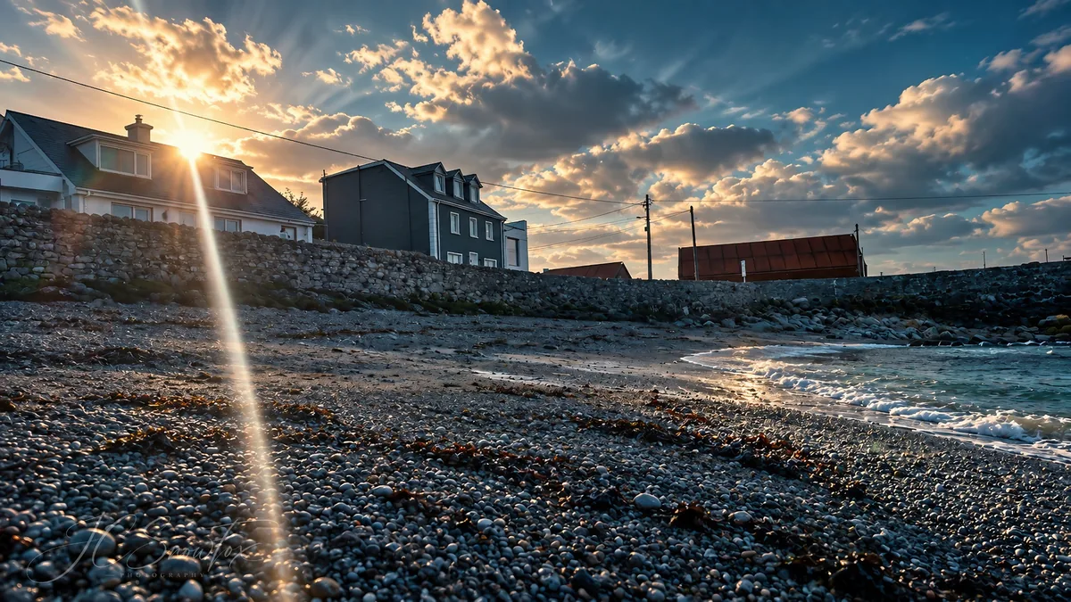 A pebble beach and seawall lit by low golden light