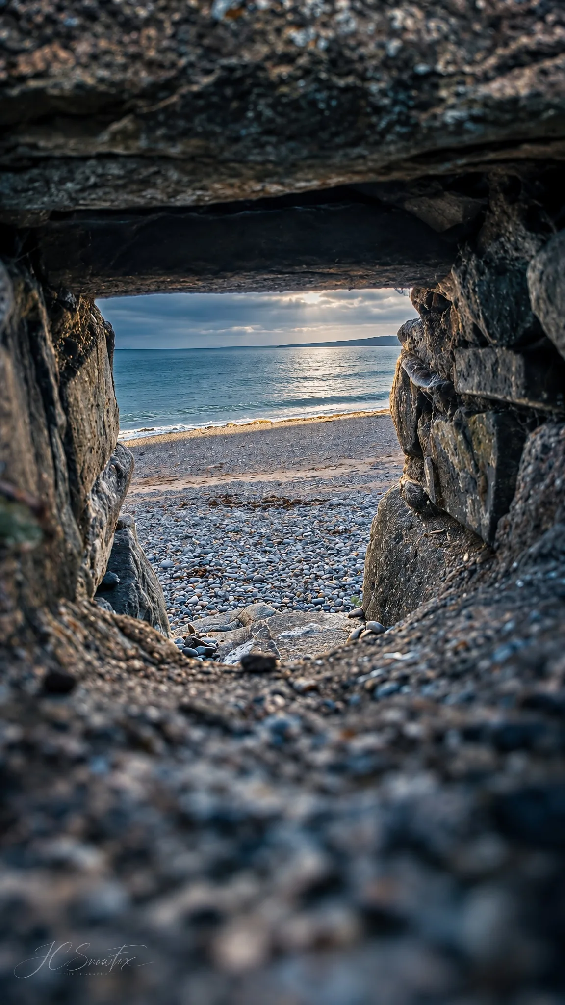 The sea framed through a small opening in a rough stone wall