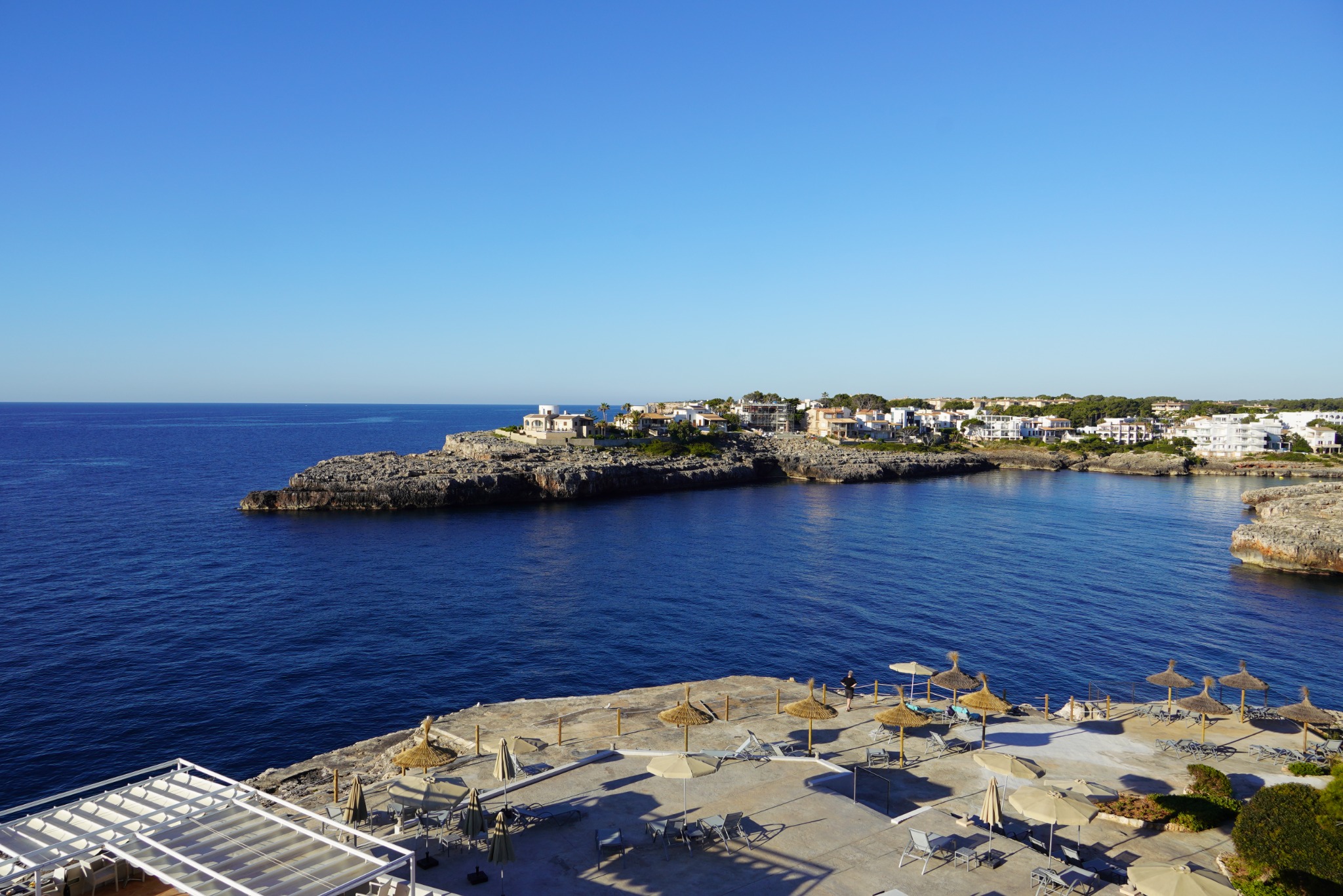 A Mediterranean cove with clear blue water, rock shelves and white buildings