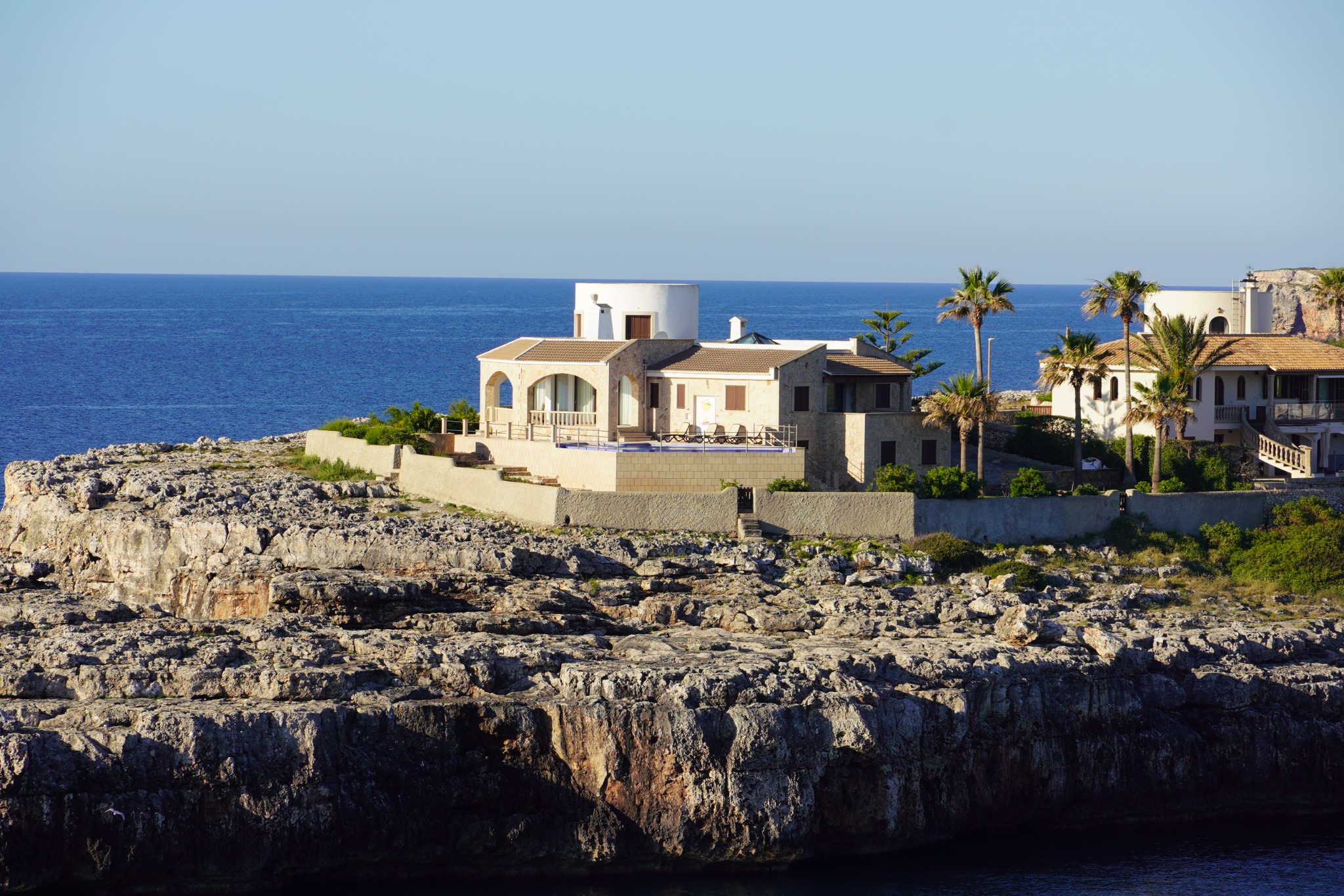 A Mediterranean villa above a rugged rocky shoreline and blue sea