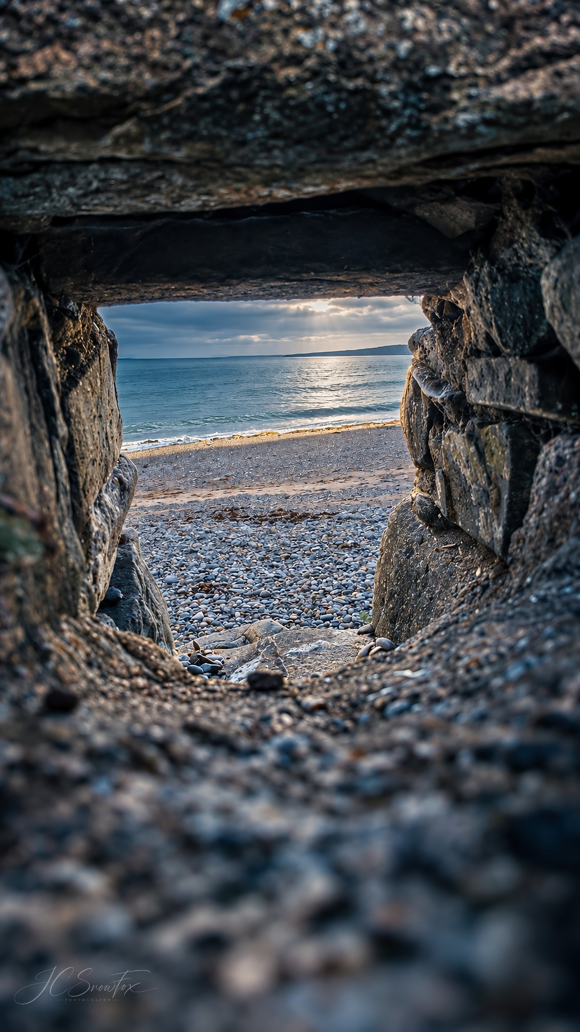 The sea seen through a small opening in a rough stone wall